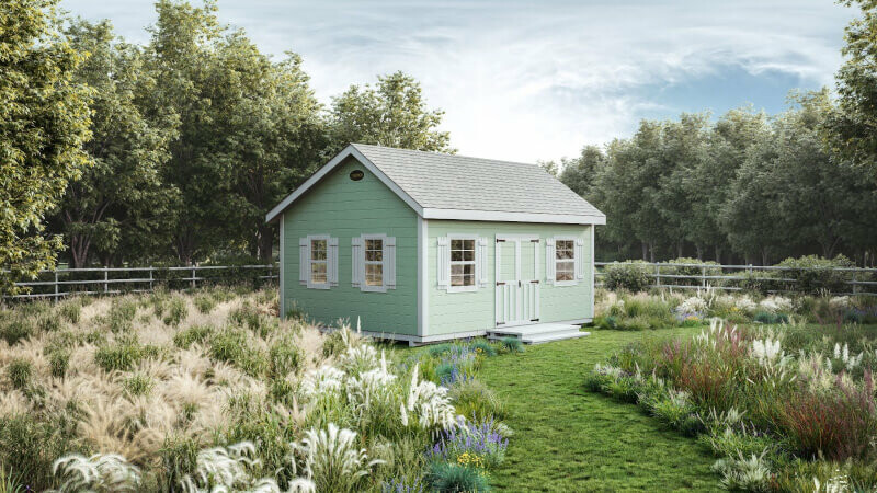 A light green Garden Cottage style storage shed from Ulrich sits in a lush garden within a fenced-in yard.